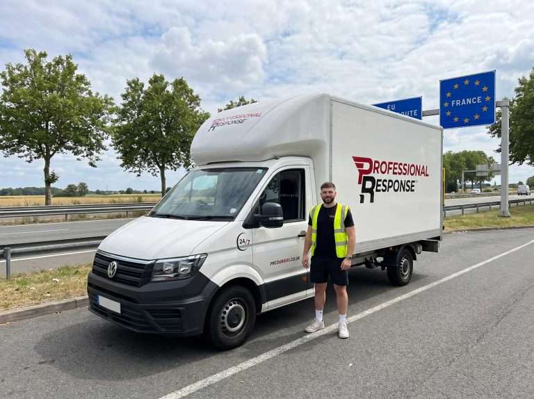 Professional Response branded Luton van parked in a French highway layby near Calais, with a driver in hi-vis vest standing beside the vehicle next to an EU France border entry sign, illustrating the company's mainland Europe delivery service